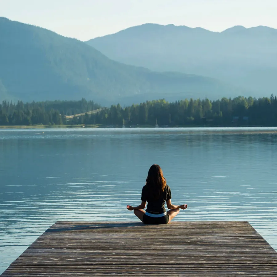 Person meditating on a dock by the water at sunrise